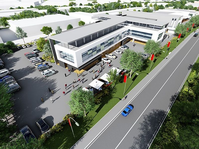 Aerial view of a modern commercial retail complex featuring a multi-story building, extensive asphalt parking facilities, and landscaped surroundings.