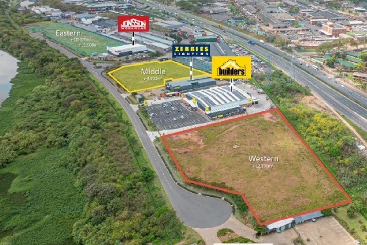Aerial view of a commercial retail development site featuring multiple plots, existing retail buildings, and paved parking infrastructure adjacent to a major highway.