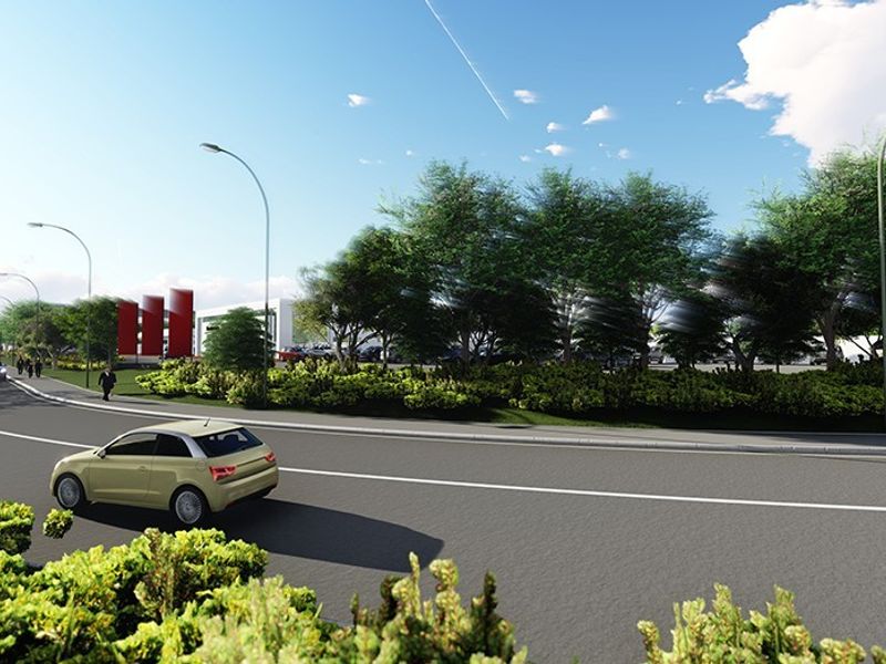 A street-level view showing the road infrastructure, landscaped verge, and street lighting leading toward the property entrance.