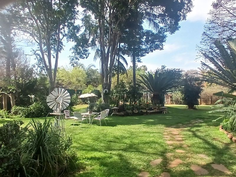 A spacious, well-established garden featuring mature trees, lush lawn, and a stone pathway, offering a serene outdoor environment.