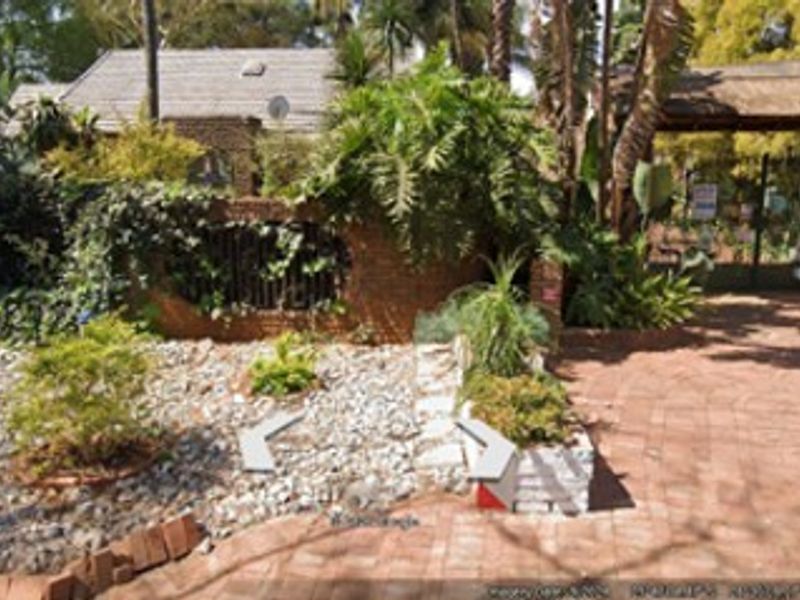 Front entrance area featuring a brick driveway, a thatched roof structure, and established garden landscaping with a brick boundary wall.