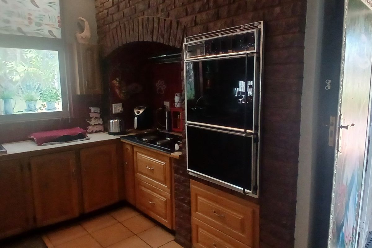 A functional kitchen featuring exposed brickwork, wooden cabinetry, a built-in double oven, and a sink overlooking the garden area.