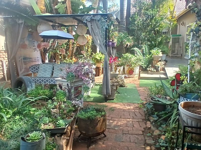 A lush, established garden area featuring a brick pathway, a covered outdoor seating structure, and mature landscaping adjacent to the main house.