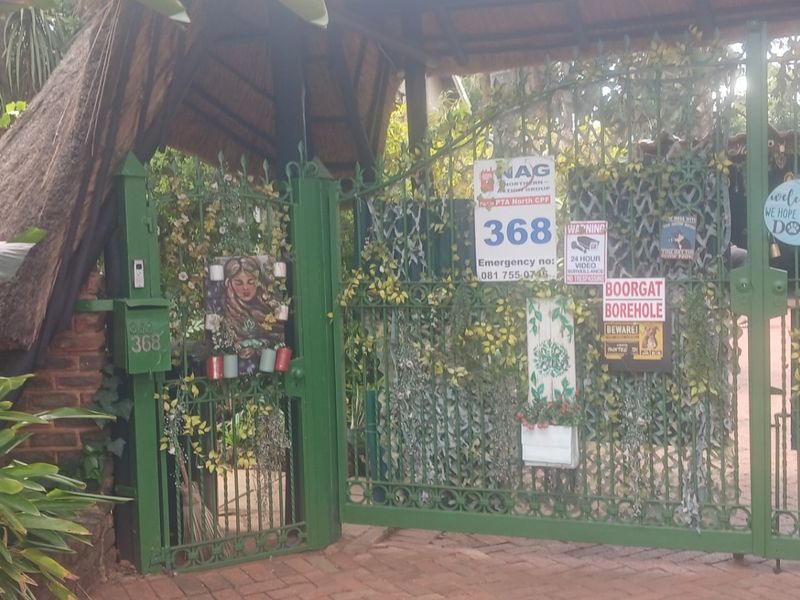 Front entrance featuring a green wrought iron gate, thatched roof structure, and brick driveway access.