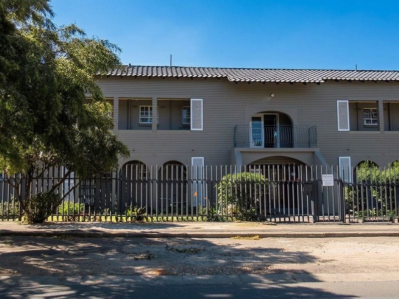 Front elevation of a two-story apartment building featuring a tiled roof, security fencing, and balcony access.