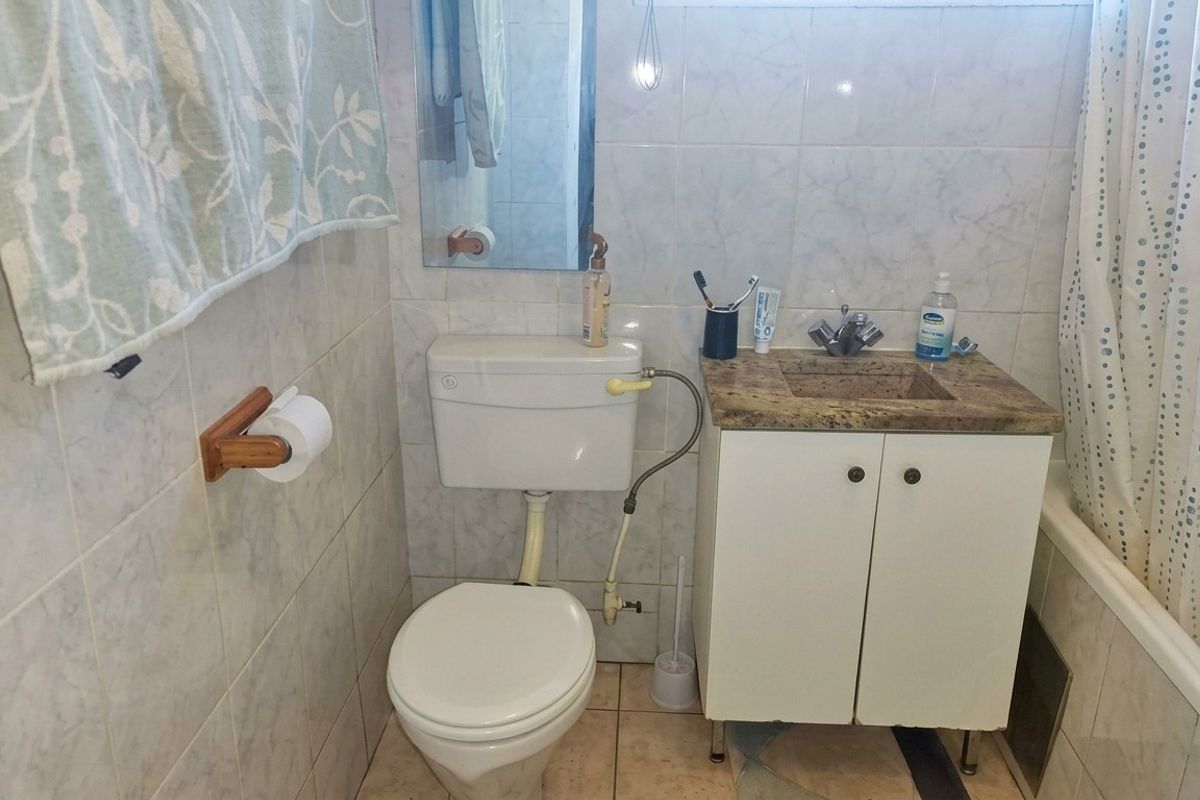 A functional bathroom featuring a vanity with stone countertop, toilet, and a combined bathtub and shower area with full-height wall tiling.