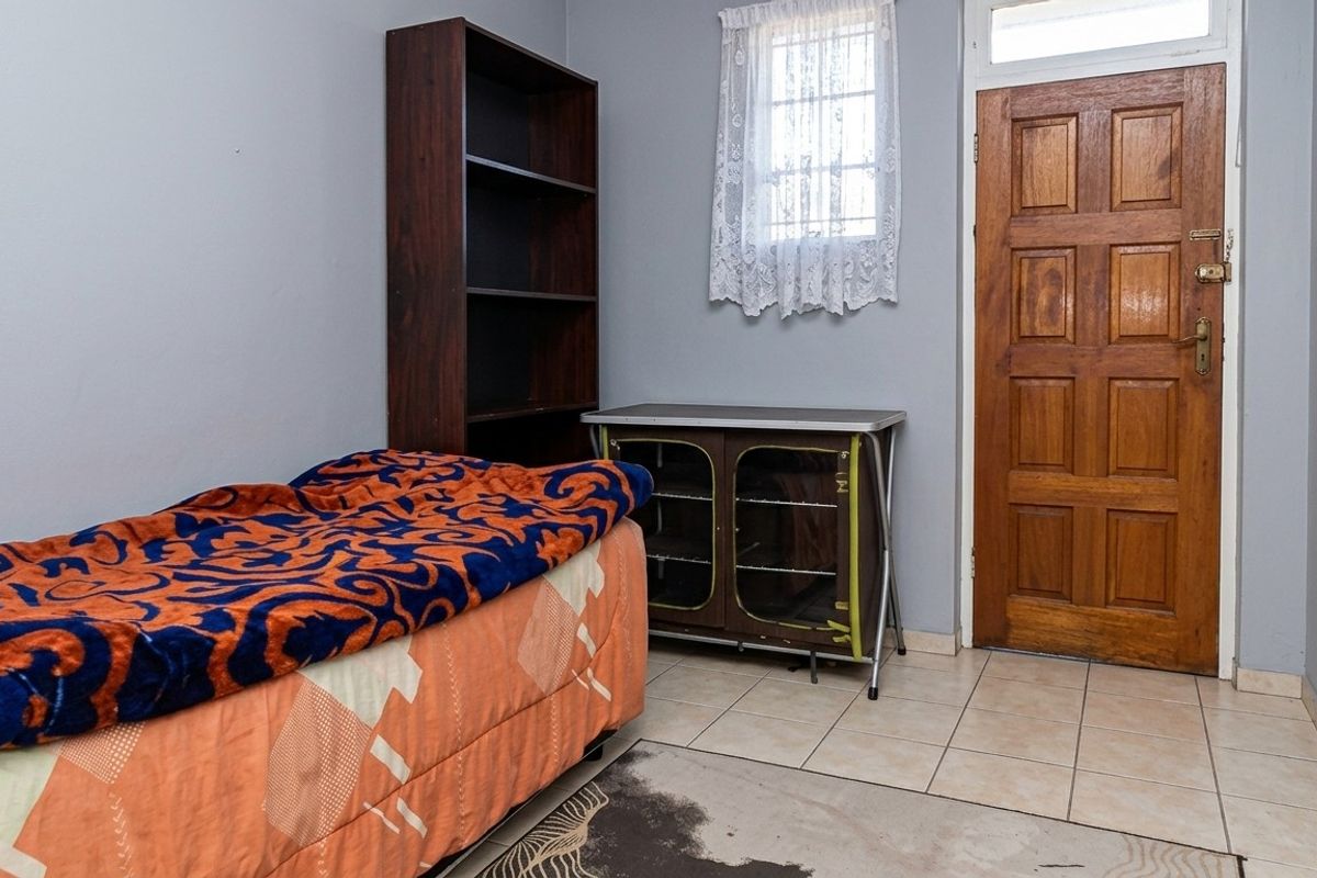 A bedroom featuring tiled flooring, a timber panel door, and a window with security bars.
