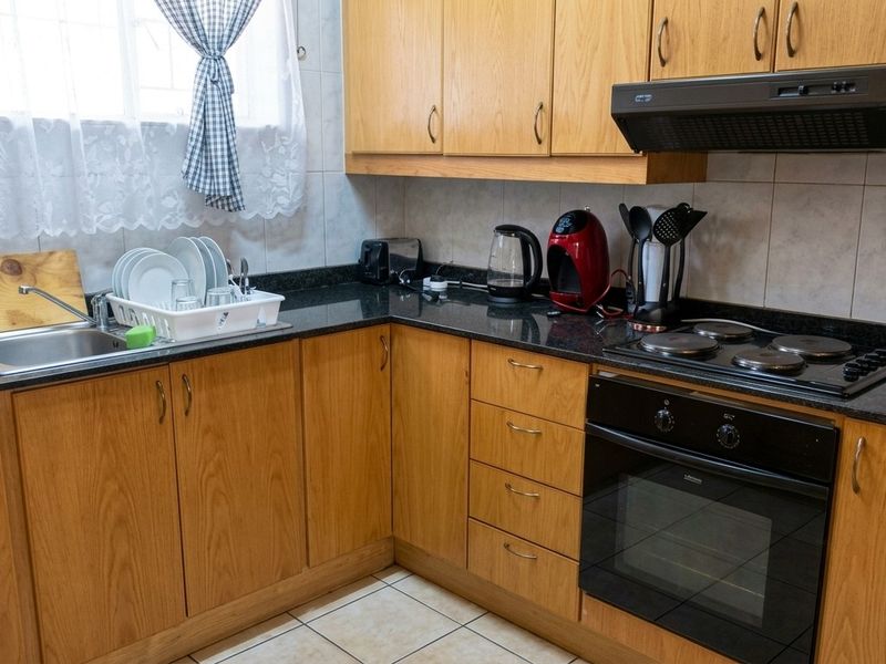 A functional kitchen featuring wood-finish cabinetry, dark granite countertops, a built-in oven with electric hob, and tiled flooring.