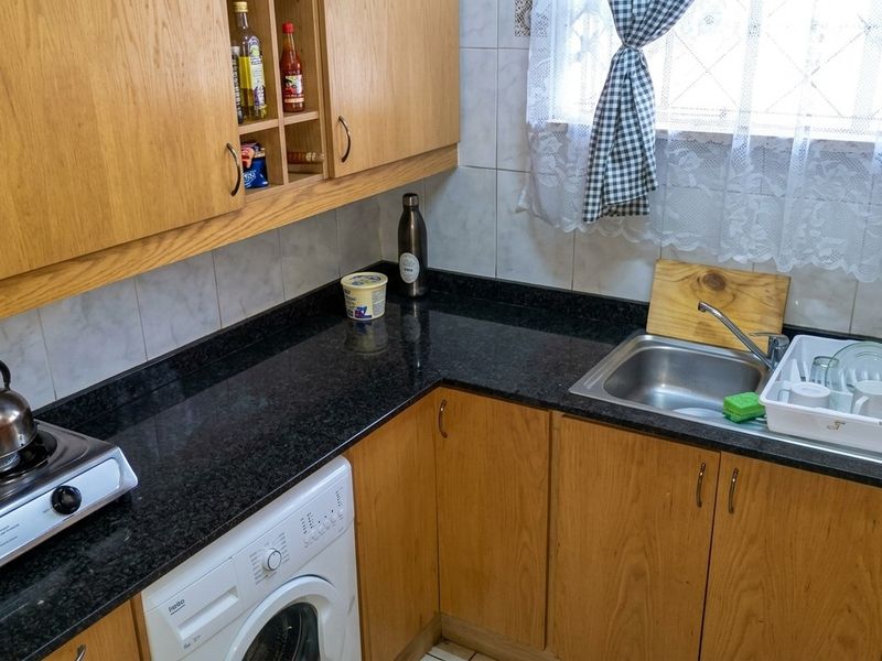 Compact kitchen featuring laminate cabinetry, granite countertops, tiled backsplash, stainless steel sink, and a built-in hob with an integrated washing machine.
