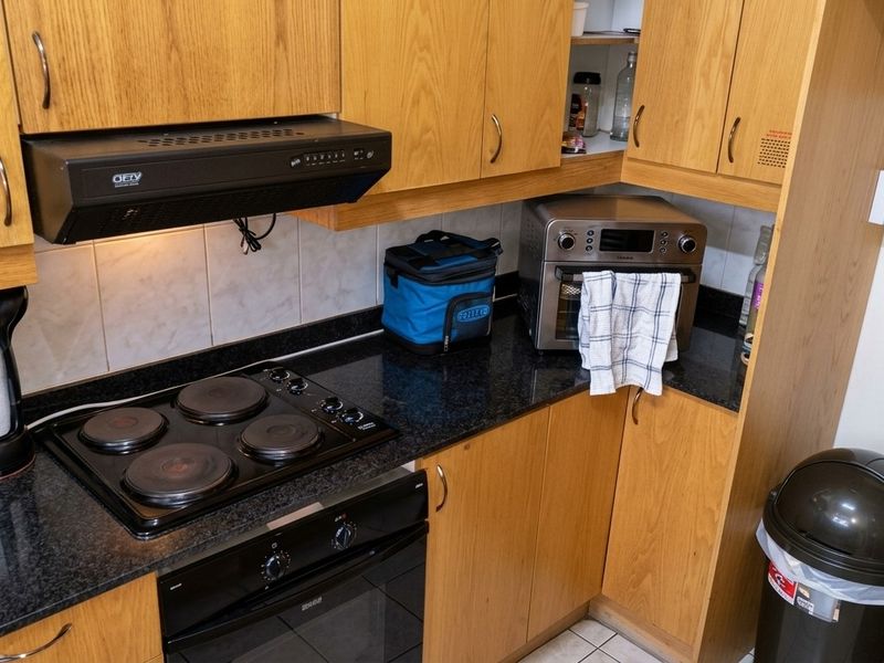 Compact kitchen featuring wood-finish cabinetry, granite countertops, a built-in electric oven, and a hob with an overhead extractor fan.