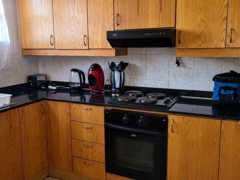 A functional kitchen featuring wooden cabinetry, black granite countertops, a built-in oven, and an electric hob with an extractor fan.