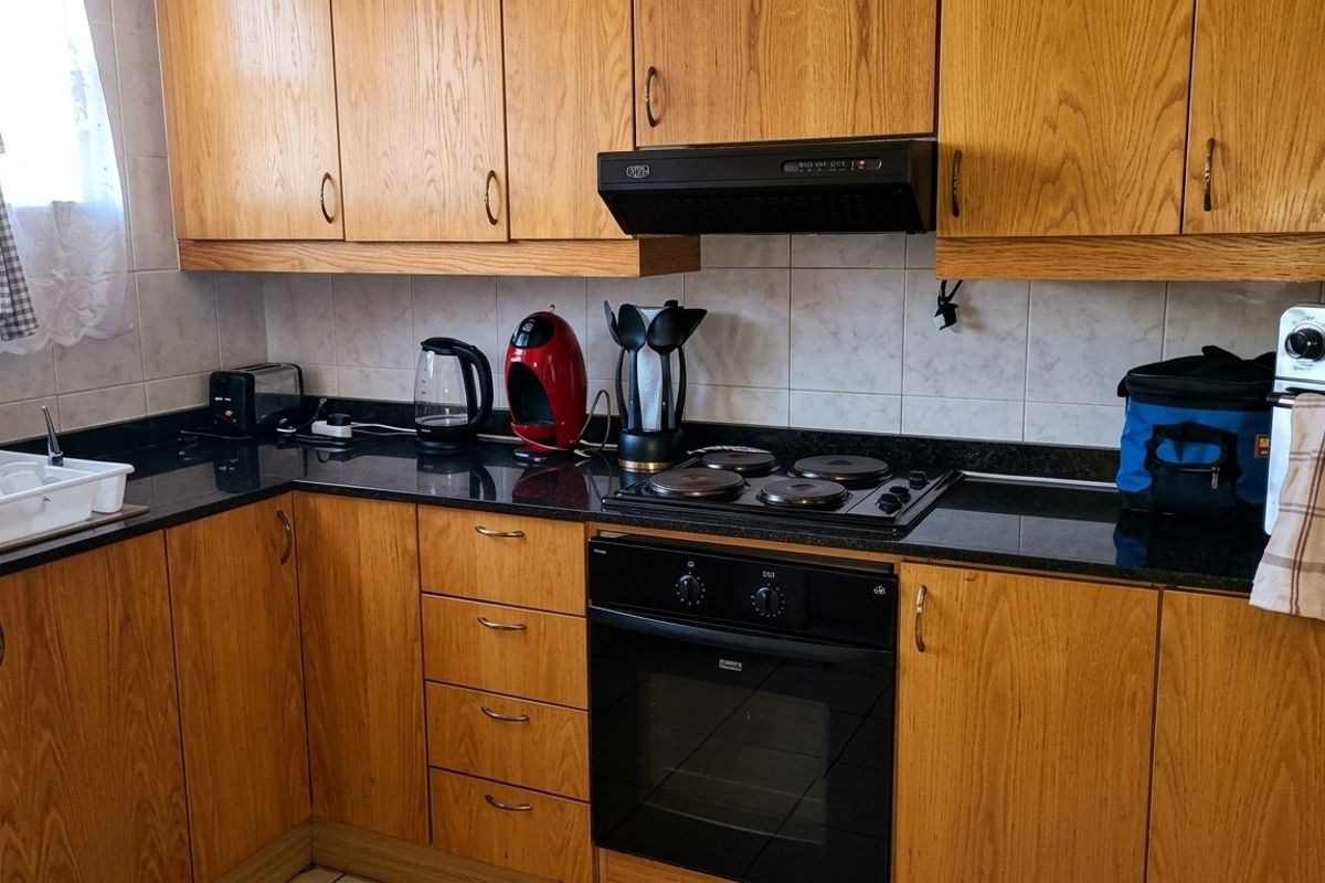 A functional kitchen featuring wooden cabinetry, black granite countertops, a built-in oven, and an electric hob with an extractor fan.
