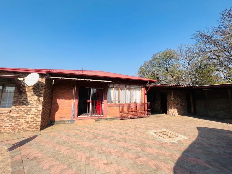 Rear view of a face brick house featuring a paved courtyard, corrugated metal roofing, and secure sliding door access.