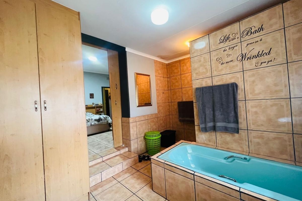 A dated bathroom featuring a built-in bathtub, tiled finishes, and integrated wooden cupboards, with visible signs of ceiling water damage.