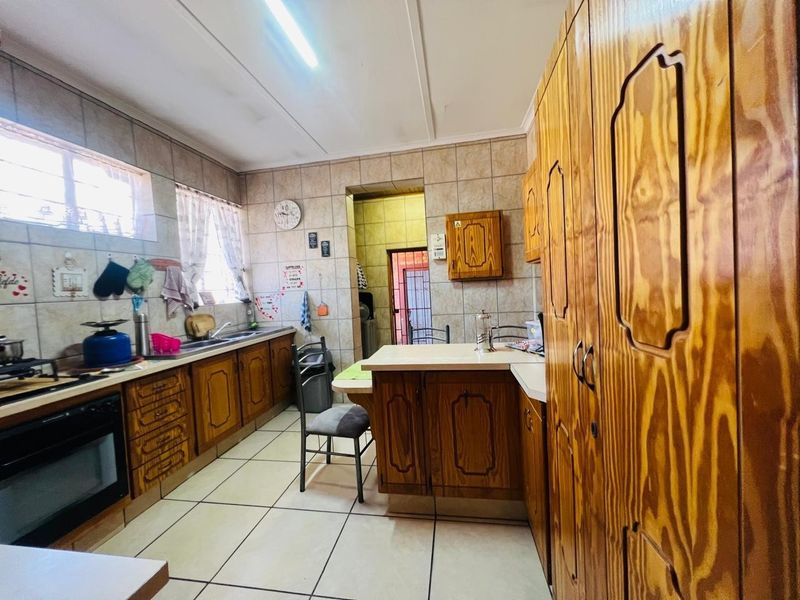 A functional kitchen featuring traditional wooden cabinetry, tiled flooring, and tiled wall finishes with built-in oven and ample counter space.