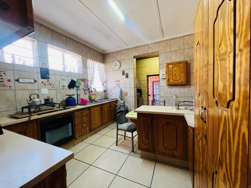 A functional kitchen featuring traditional wooden cabinetry, tiled backsplash, and tiled flooring, offering a classic layout with ample storage and workspace.