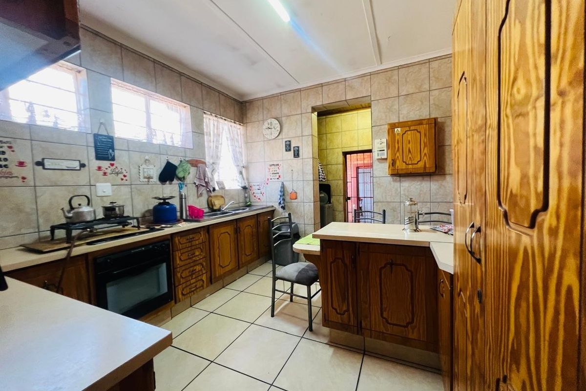 A functional kitchen featuring traditional wooden cabinetry, tiled backsplash, and tiled flooring, offering a classic layout with ample storage and workspace.