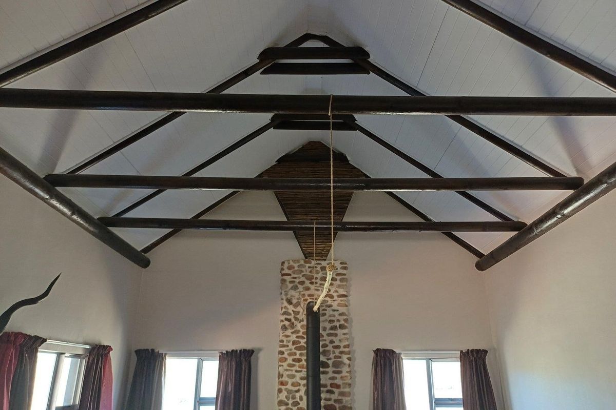 Spacious living area featuring a high vaulted ceiling with exposed timber rafters and a prominent stone-clad fireplace with a wood-burning stove.