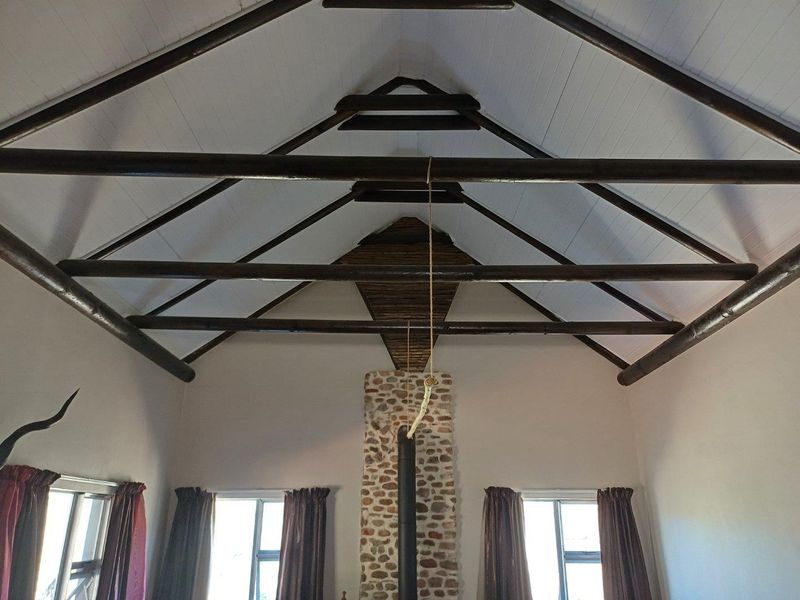Spacious living area featuring a high vaulted ceiling with exposed timber rafters and a prominent stone-clad fireplace with a wood-burning stove.