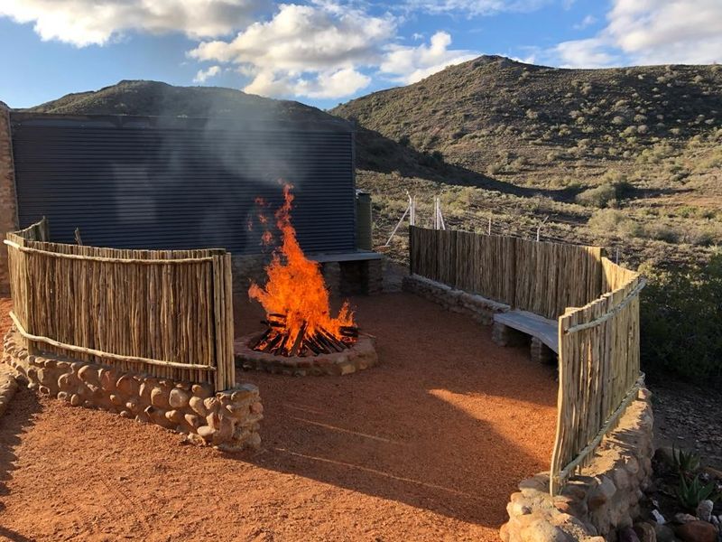 Outdoor entertainment area featuring a stone fire pit, built-in stone seating, and rustic timber fencing set against a scenic mountain landscape.