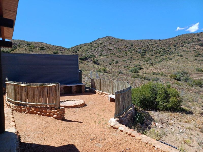 Outdoor patio area featuring a stone-built fire pit, stone retaining walls, and reed fencing, set against a scenic mountain landscape.