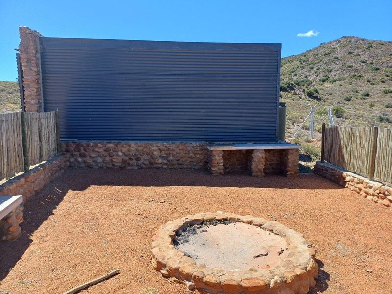 Outdoor entertainment area featuring a stone fire pit, built-in stone seating, and a corrugated metal privacy wall set against a natural landscape.