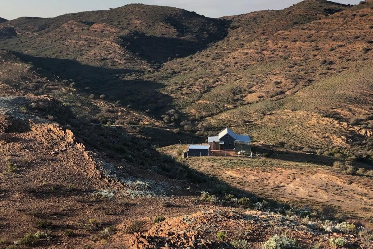 An aerial view of a remote house situated in a vast, rugged mountainous landscape.