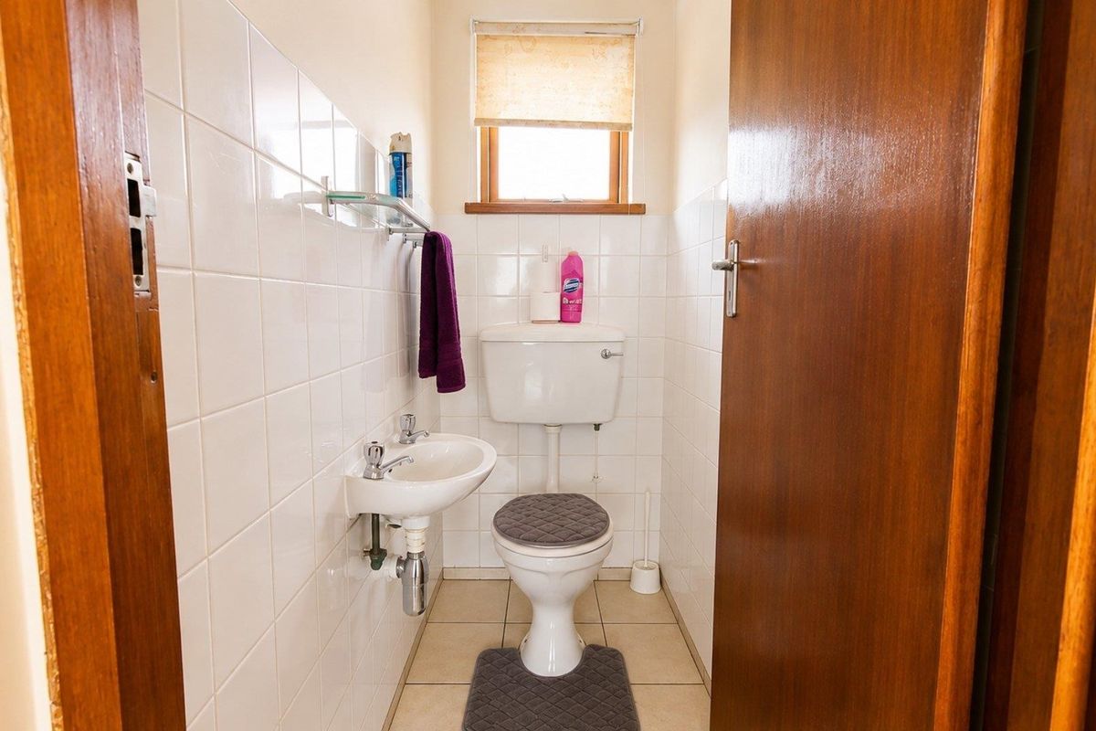 A compact guest bathroom featuring a wall-mounted basin, ceramic toilet, and neutral wall tiling, providing a functional and clean space.