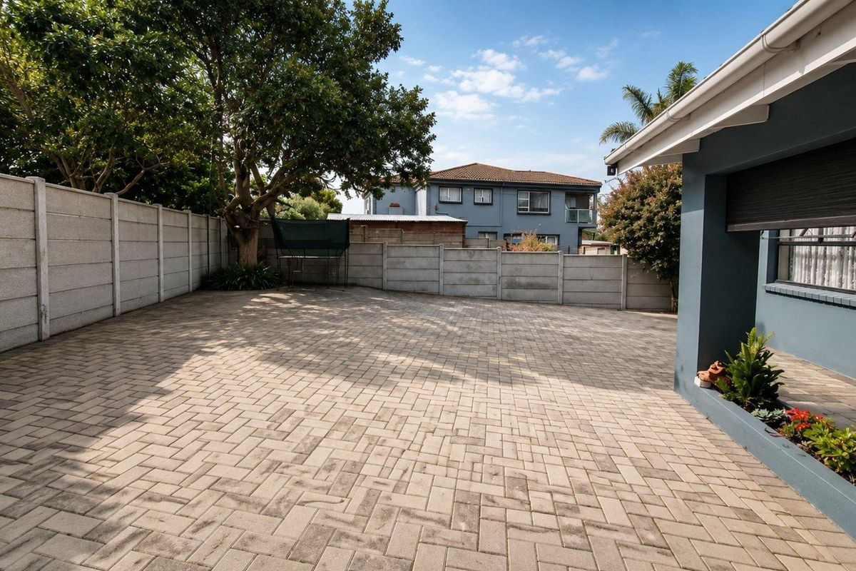 A spacious paved rear courtyard featuring a secure precast concrete boundary wall, mature trees, and a built-in planter box along the house exterior.