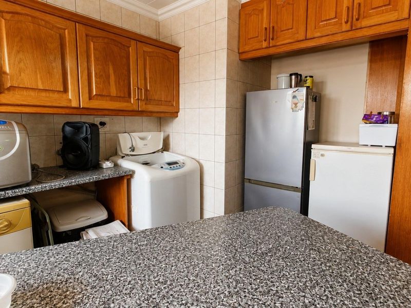 A functional laundry area featuring built-in wooden cabinetry, durable laminate countertops, and tiled splashbacks, providing ample storage and workspace for utility tasks.