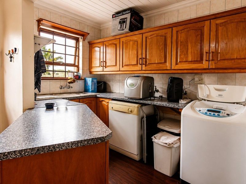 Functional laundry area featuring wooden cabinetry, laminate countertops, tiled backsplash, and a stainless steel sink with natural light from a timber-framed window.