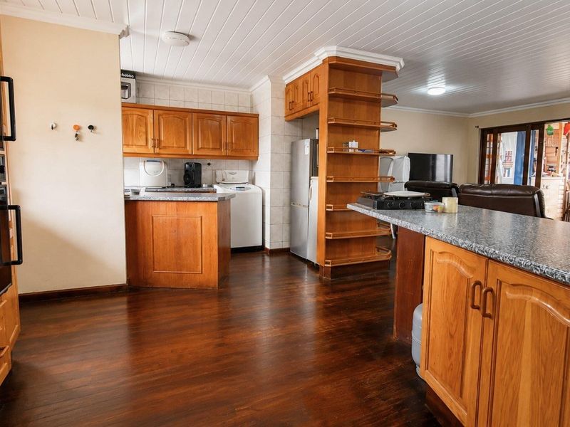 Open-plan kitchen and living area featuring warm timber cabinetry, granite countertops, a double wall oven, and rich hardwood flooring throughout.