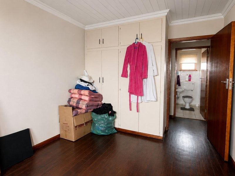 A bedroom featuring built-in cupboards, dark laminate flooring, and a tongue and groove ceiling, with an adjacent en-suite bathroom visible.