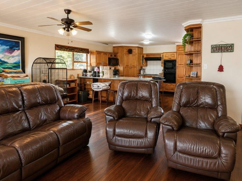 Spacious open-plan living area featuring a functional kitchen with wooden cabinetry, built-in appliances, and a breakfast bar, seamlessly connected to the lounge.