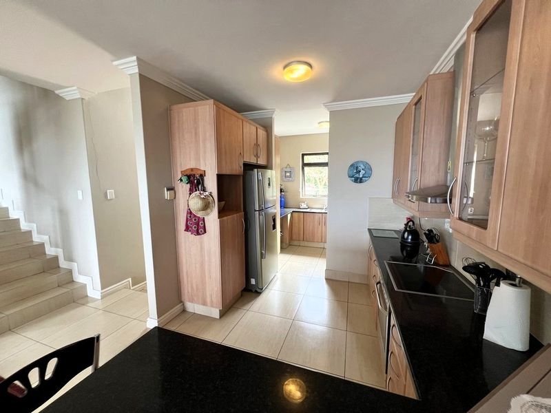 Functional kitchen featuring wood-finish cabinetry, dark granite countertops, and tiled flooring, with an adjacent staircase and open-plan layout.