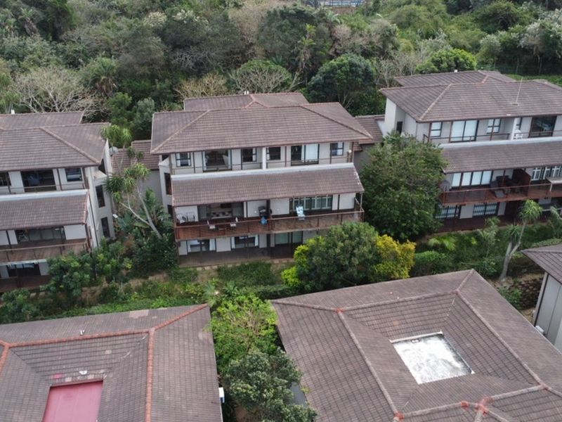 Aerial view of a residential apartment complex featuring tiled roofs, private balconies, and lush surrounding greenery.