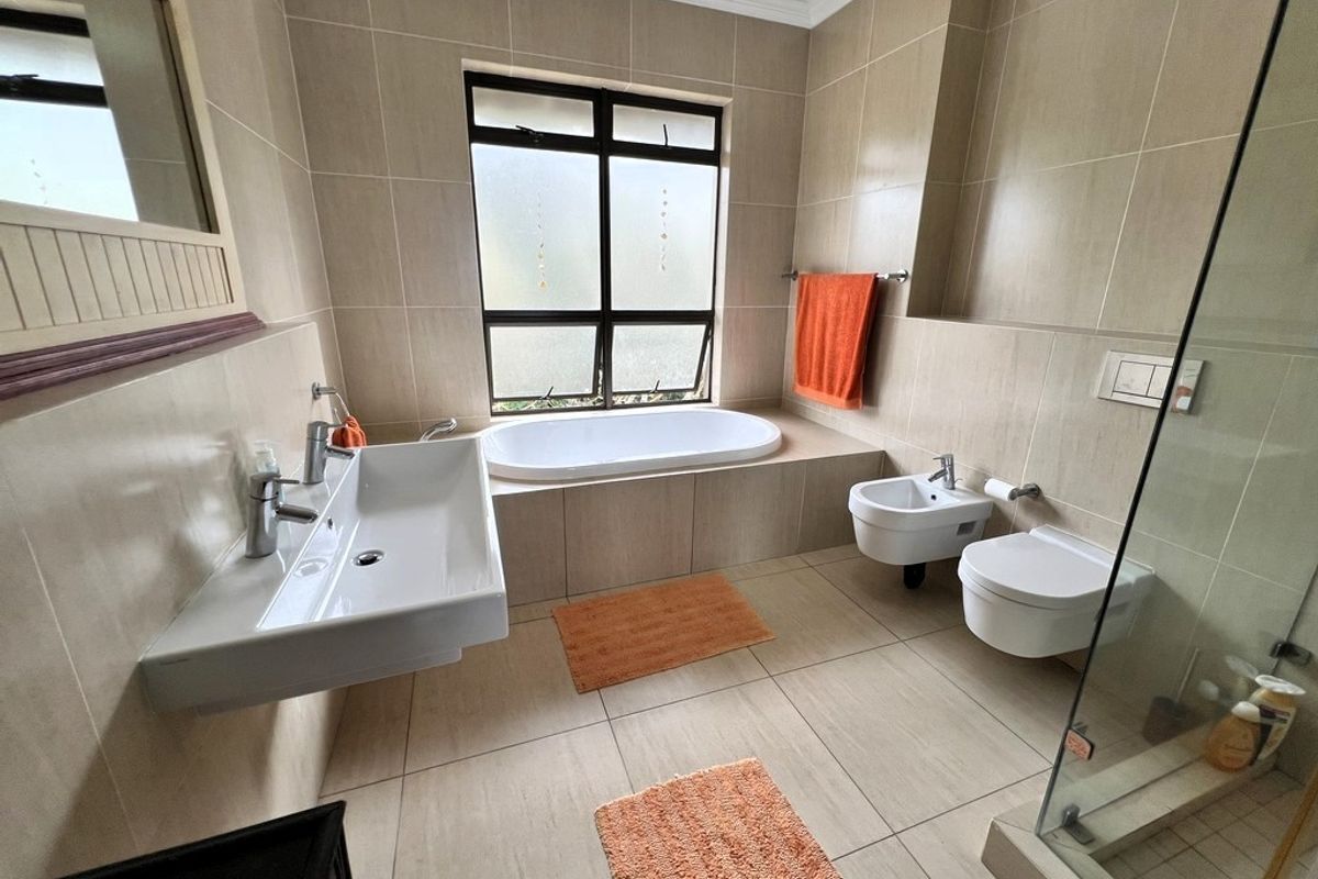 Modern bathroom featuring a wall-mounted basin, built-in bathtub, wall-hung toilet, bidet, and a glass-enclosed shower with neutral floor-to-ceiling tiling.