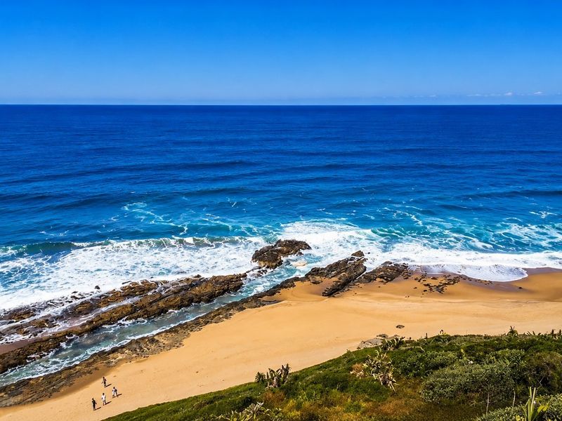 A scenic elevated view of the coastline, featuring sandy beach, rocky outcrops, and the ocean.