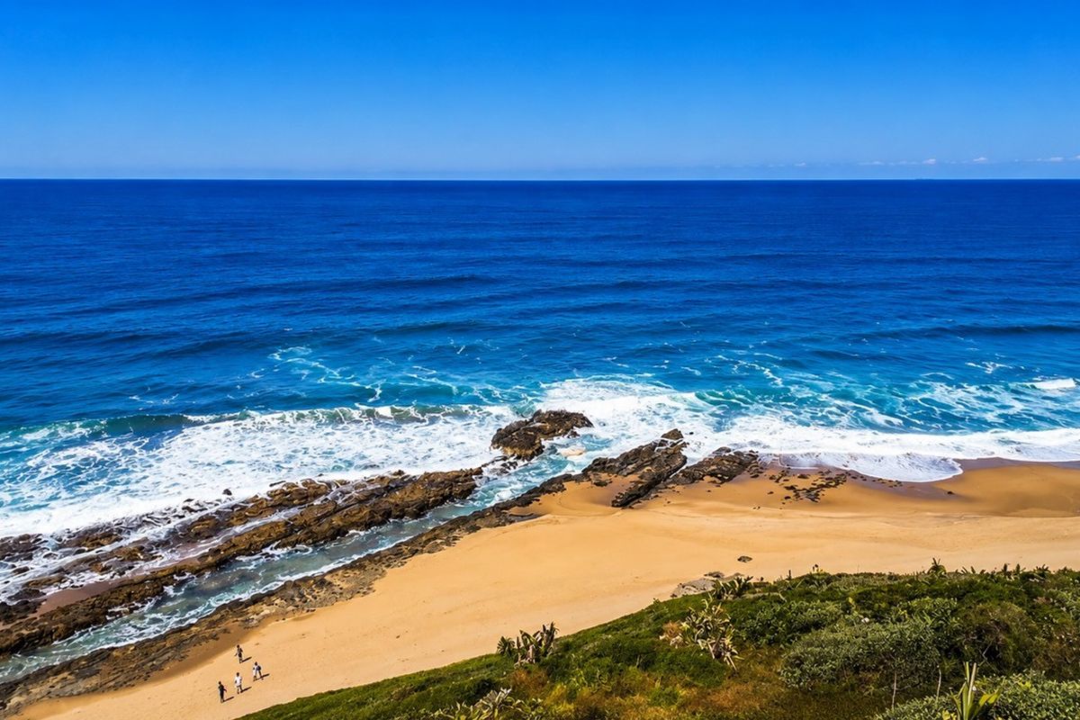 A scenic elevated view of the coastline, featuring sandy beach, rocky outcrops, and the ocean.