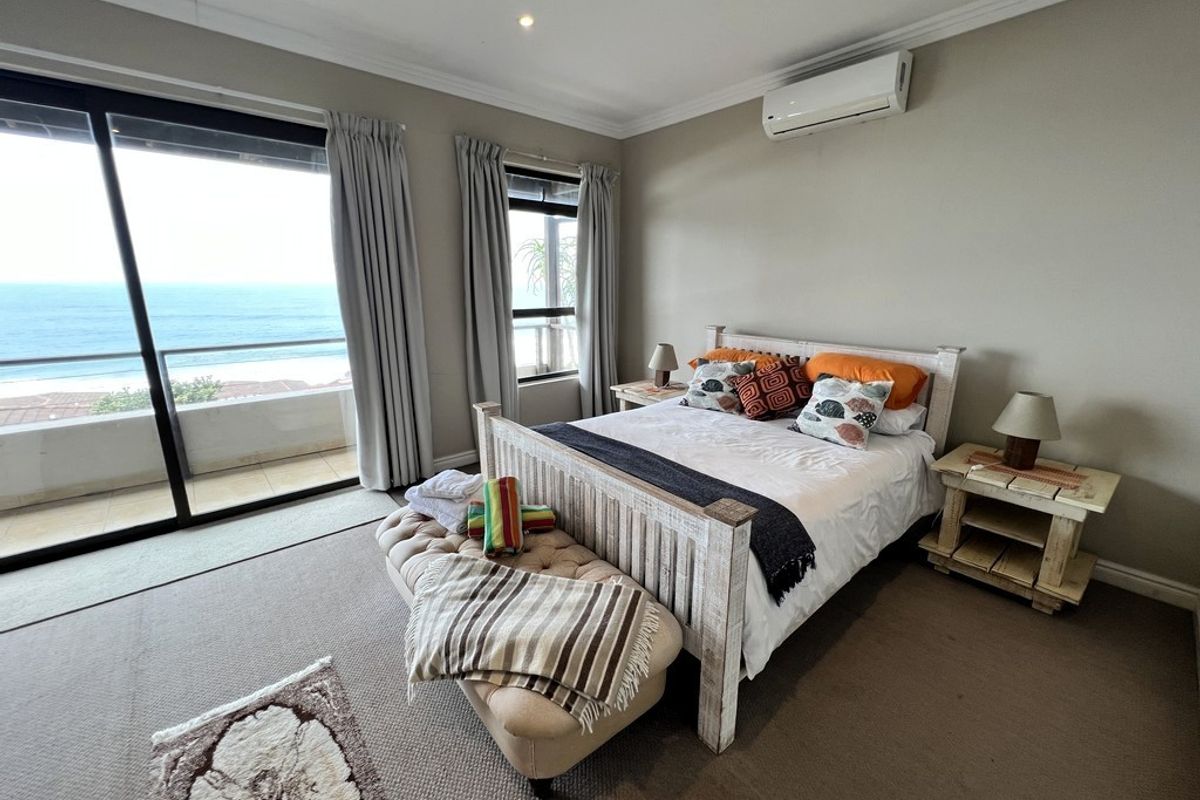 Spacious bedroom featuring carpeted flooring, a wall-mounted air conditioning unit, and large sliding glass doors providing direct access to a balcony with ocean views.
