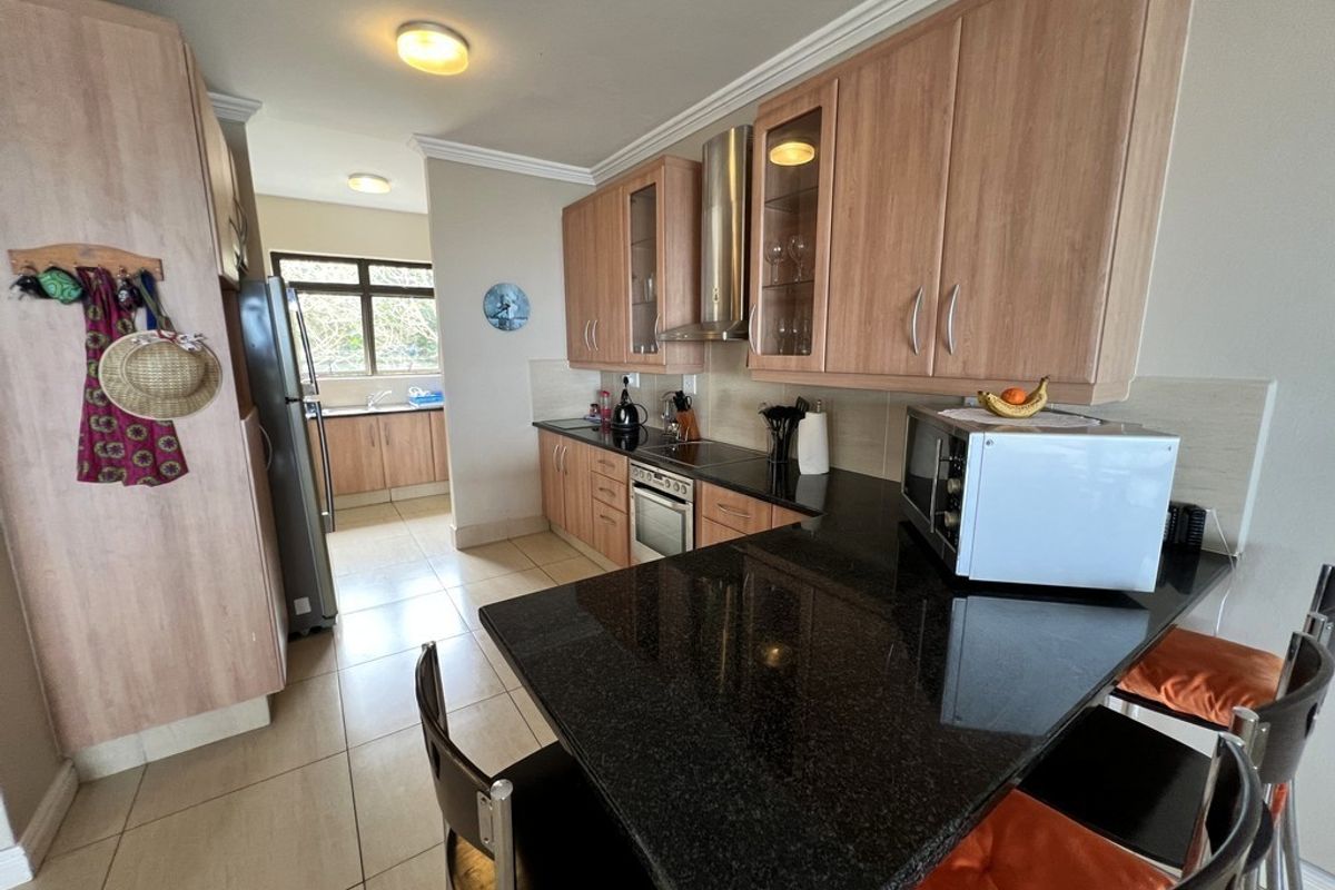 A functional kitchen featuring granite countertops, wood-finish cabinetry, a built-in oven with extractor fan, and a convenient breakfast bar area.