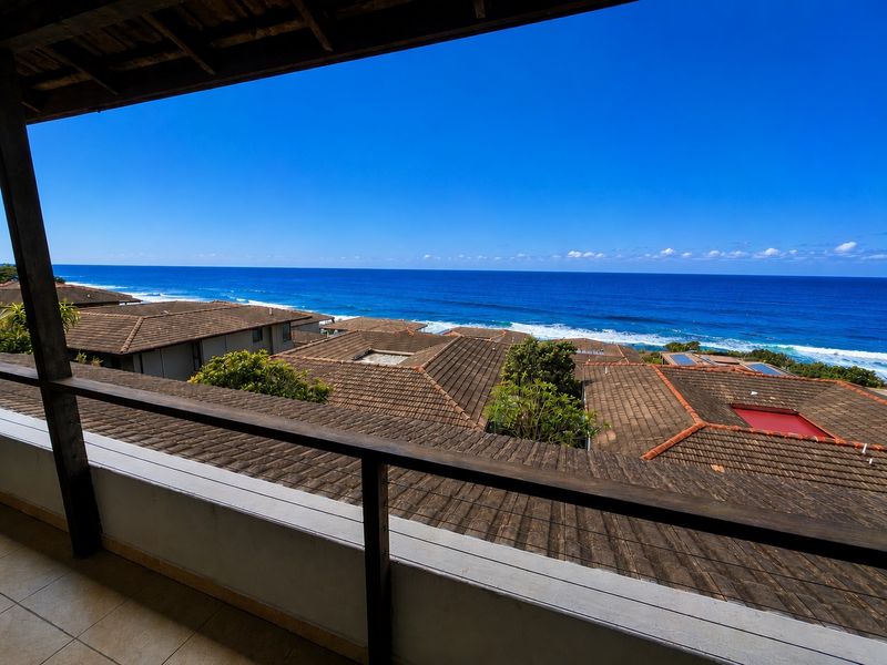 Covered balcony featuring tiled flooring and timber railings, offering expansive, elevated views of the ocean and surrounding coastal rooftops.