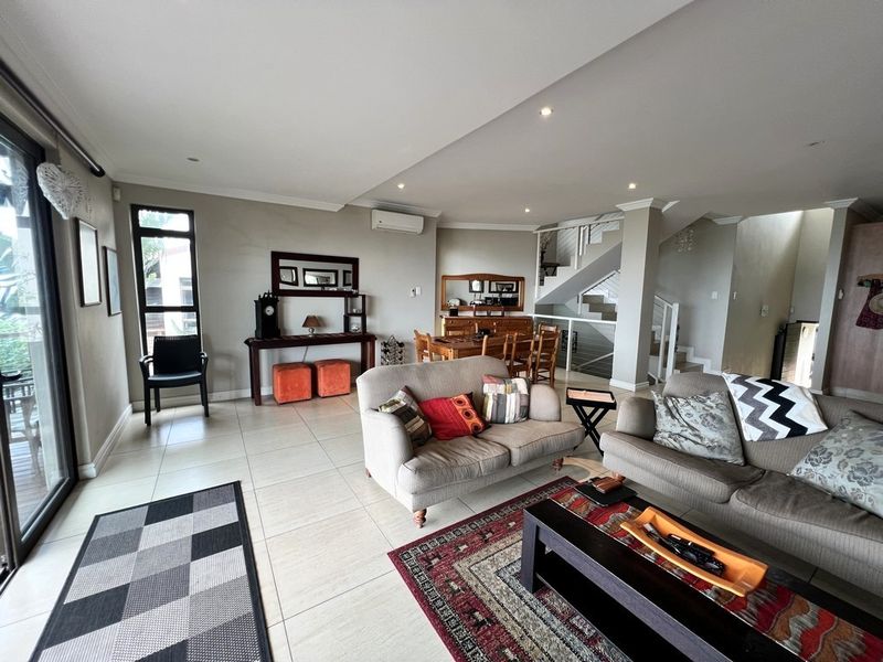 Spacious open-plan living and dining area featuring tiled floors, recessed lighting, a split-system air conditioner, and a modern staircase with glass balustrades.
