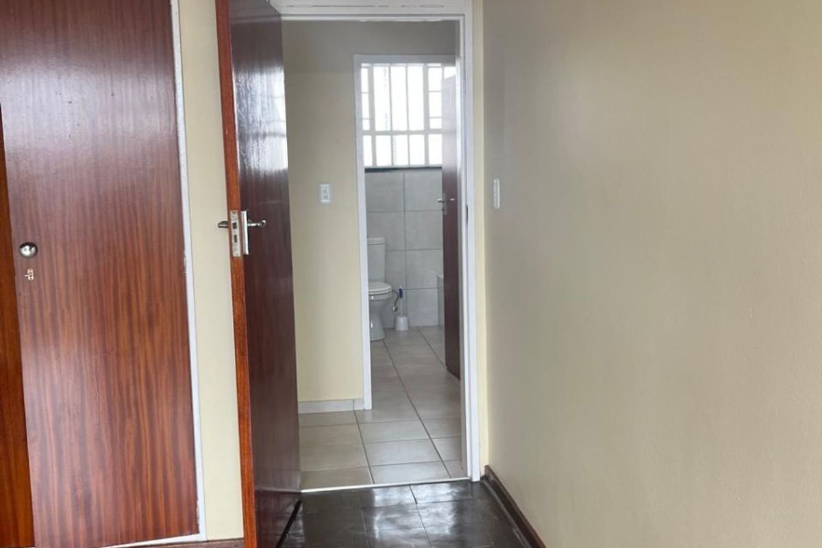 A bedroom featuring built-in cupboards and original parquet flooring, with an adjoining bathroom visible through the doorway.