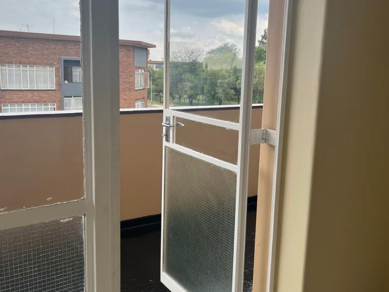 A simple balcony area accessed through a metal-framed glass door, featuring tiled flooring and a standard safety railing.