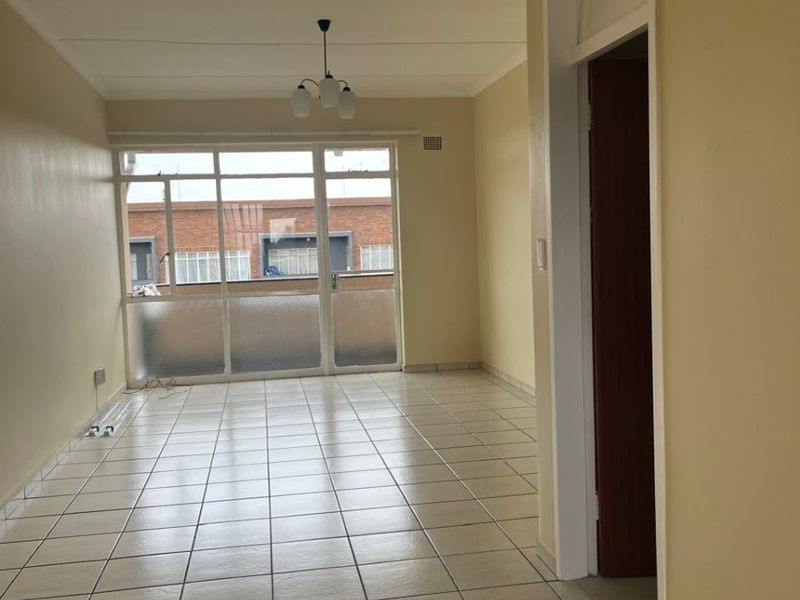 A bright, empty living area featuring neutral tiled flooring and a large glass sliding door leading to an outdoor space.