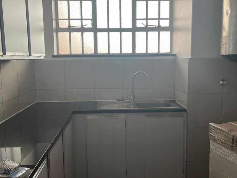A functional kitchen area featuring built-in cabinetry, a stainless steel sink, tiled backsplash, and tiled flooring with natural light from a window.