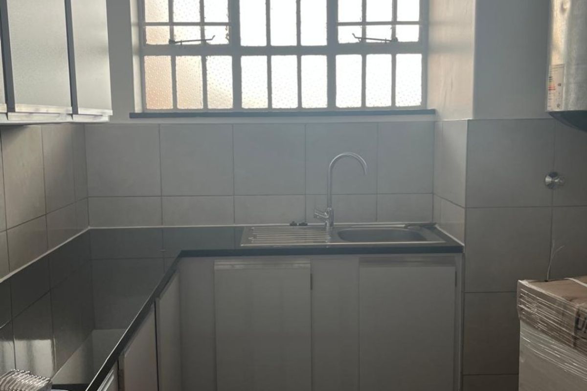 A functional kitchen area featuring built-in cabinetry, a stainless steel sink, tiled backsplash, and tiled flooring with natural light from a window.