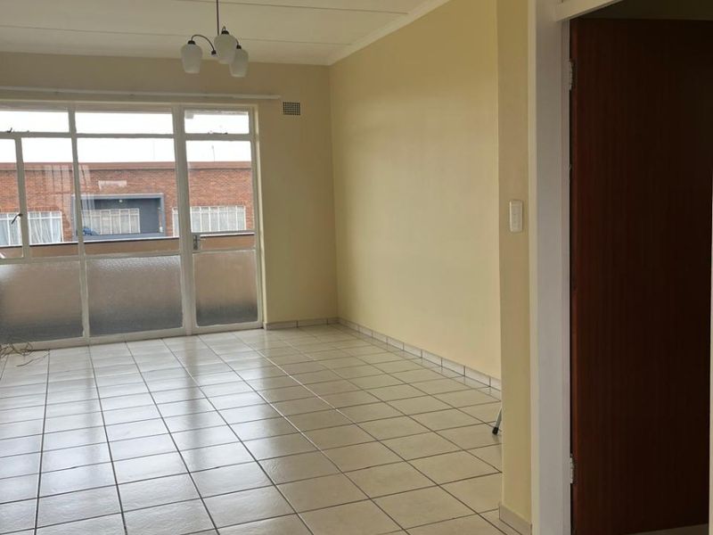 A bright, empty living room featuring neutral tiled flooring and a large sliding glass door providing access to an outdoor balcony area.