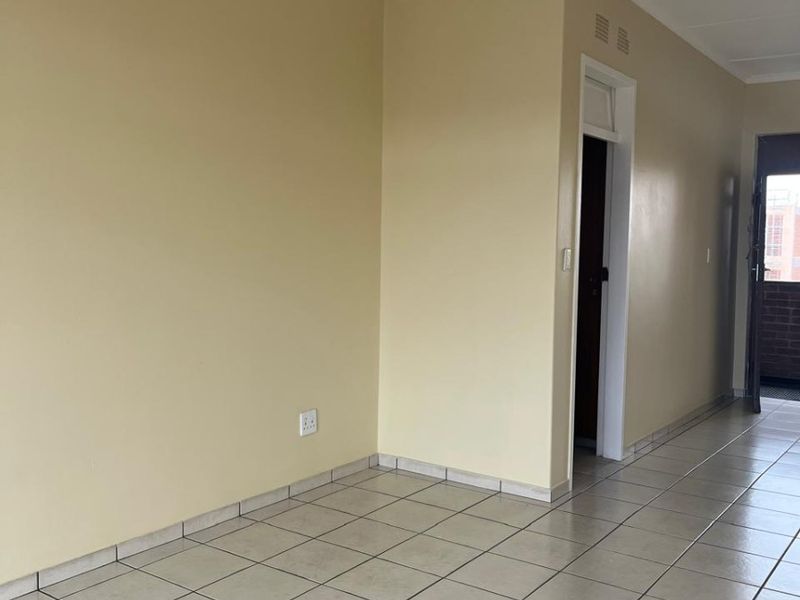 An empty living area featuring neutral wall paint, ceramic floor tiles, and a central ceiling light fixture, providing a clean and versatile space.